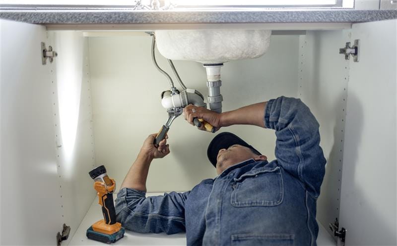 Plumber repairing pipes beneath a bathroom sink in Irvine